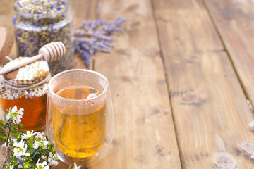 A glass with tea, spring white flowers. Bank with honey. Dried tea in a jar. Wooden background and...