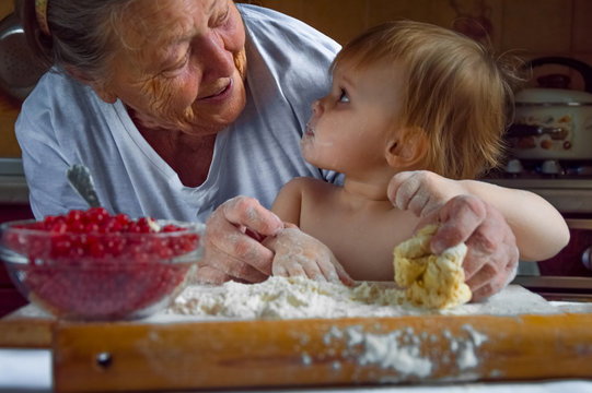 Portrait Of Faces, Hands Happy Gray-haired Granny, Granddaughter. Toddler Girl Play With Baking, Dough, Flour On Kitchen. Child Baby Try Study Cooking Cookies, Cake. Cozy Family Look At Each Other