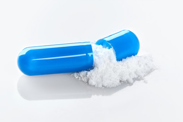 Single blue capsule on white background. Contents of the medical capsule