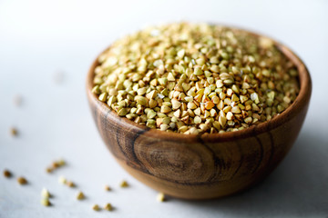 Raw organic green buckwheat in wooden bowl and rosemary on grey background. Copy space. Food ingredients.