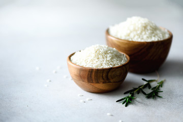 White raw organic jasmine rice in wooden bowl and rosemary on light concrete background. Food ingredients. Copy space