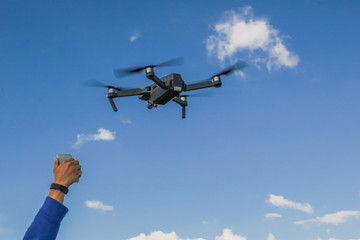 gray drone in a blue sky with clouds with a hand in which the phone is clamped to control the drone