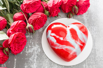 Valentines day or birthday greeting card. Cake in the form of a red heart. Red roses and dessert on vintage wooden table