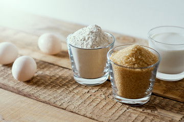 fresh milk, flour, eggs and sugar on a wooden table prepared for baking a cake