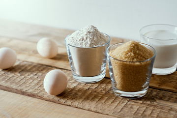 fresh milk, flour, eggs and sugar on a wooden table prepared for baking a cake