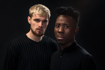 Portrait of two young african american and caucasian men standing over black background. Studio shot