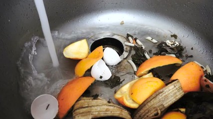 Equipment in the modern kitchen. Chopper household kitchen waste in the sink. Peel oranges, banana peels, eggshell washed with a jet of water. Slow motion.
