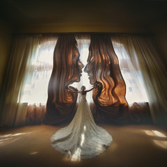 Bride opens brown curtains standing before bright window. Silhouettes of faces of a couple in love....