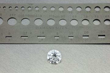Diamond : loose brilliant 4 carats diamond, next to a diamond size silver ruler with holes in background bright