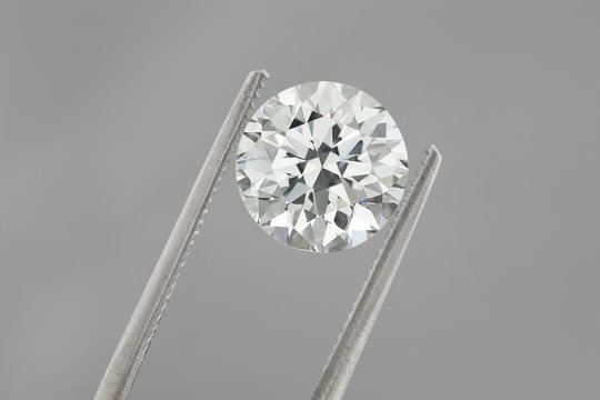 Diamond : loose brilliant 4 carats diamond is being held by a tweezers on grey silver background