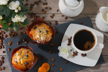 Good morning with two muffins, cup of aroma coffee, jug of cream to coffee and flowers of azalia on gray wooden background. Top view.