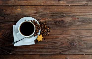 A cup of coffee, coffee beans and one star cookies on wooden background, copyspace.