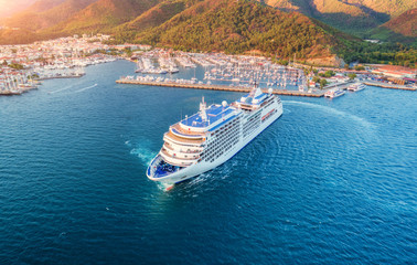 Cruise ship at harbor. Aerial view of beautiful large white ship at sunset. Colorful landscape with boats in marina bay, sea, green forest. Top view from drone of yacht. Luxury cruise. Floating liner