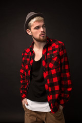 Handsome trendy young guy at the studio on black background. He wears beard and a plaid shirt