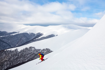 A man is skiing on the slope, wearing brigh  red yellow jumpsuit.