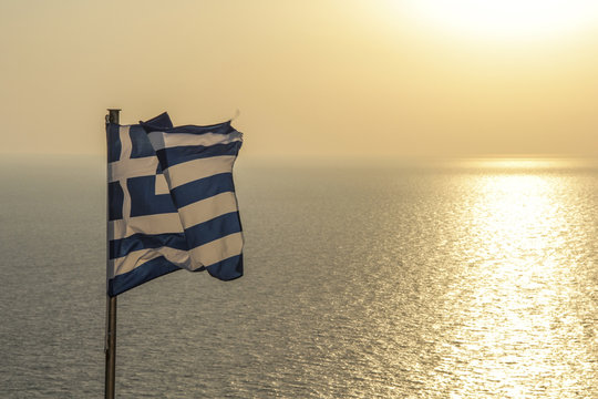 Greek Flag waving by sea against sky during sunset