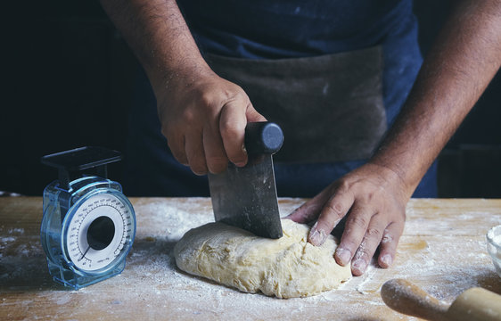 Midsection of man cutting dough at table in bakery