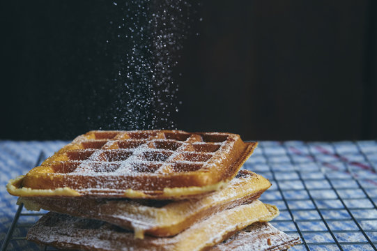 Close-up of powdered sugar sprinkling on waffle against black background