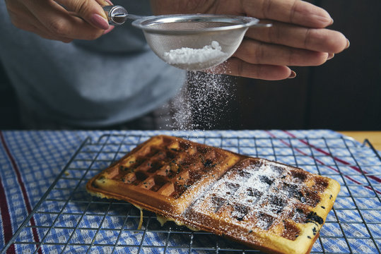 Midsection of woman sprinkling powdered sugar on waffle at table
