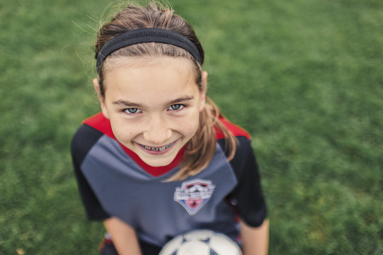 Portrait of smiling girl holding soccer ball while sitting on field