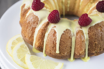 Lemon cake frosted with yellow sugar icing and red raspberries, dressed with lemon slices on the side on a white platter