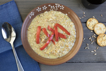 Farro grain soup dressed with red peppers and service in a brown ceramic bowl with a blue napkin and gold sppon and crackers