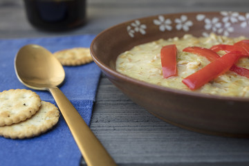 Farro grain soup dressed with red peppers and service in a brown ceramic bowl with a blue napkin and gold sppon and crackers