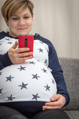 Obraz premium Schwangere Frau schaut auf ein Smartphone