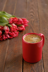 red coffee cup with tulips on dark wood background