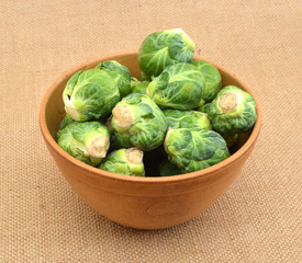 freshly brussel sprouts and some whole ones in wooden bowl on burlap background