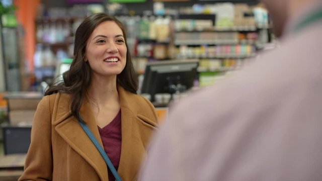 Handheld shot of female customer talking to worker at checkout counter in store