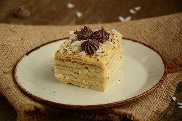 Piece of cake napoleon on a plate with chocolate candys,  custard and coconut chips  