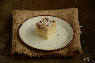 Piece of cake napoleon on a plate with chocolate candys,  custard and coconut chips  