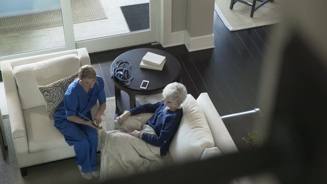High angle dolly shot of senior woman and home caregiver using tablet computer in living room