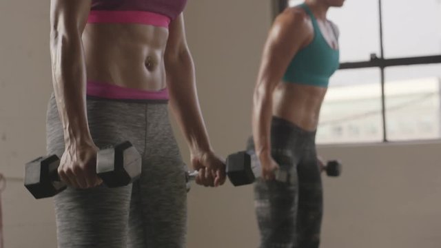 Handheld shot of female athletes exercising jump squats with dumbbells in gym
