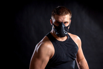 Portrait of a dark-haired man athlete in a black training mask, a sports shirt on a black isolated background