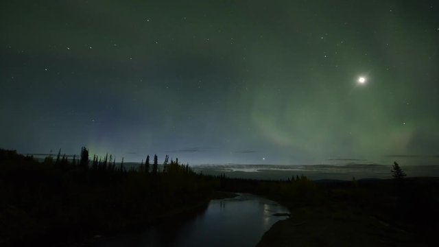 Time lapse shot of aurora borealis over landscape against star field at night