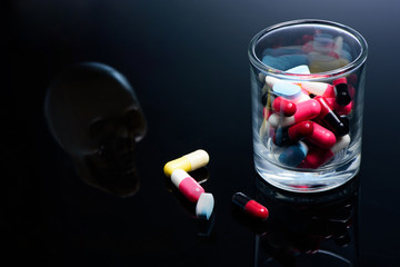 Pills and medicine capsule and skull on reflex table over dose concept