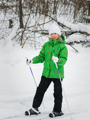 Little girl in a bright green suit learns to ski in the woods.