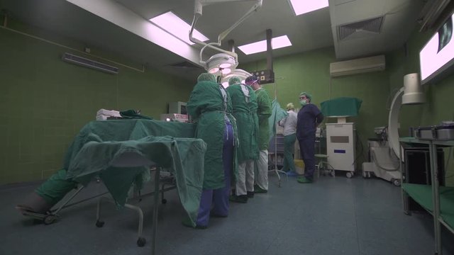 Crane shot from medical tools and instruments on tray to surgeon team performing surgery at operation theatre, doctor specialist operating patient, surgical procedure of hip replacement, crane shot