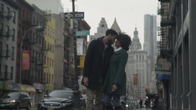 Handheld shot of couple kissing while walking on footpath in city