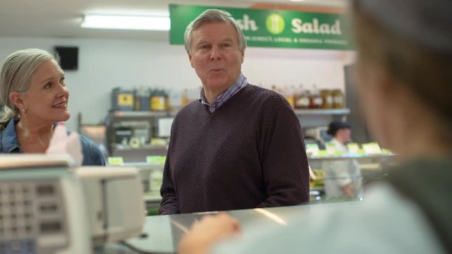 Handheld shot of worker giving packet to senior customers at supermarket