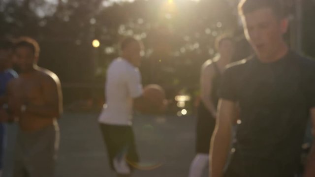 Handheld shot of happy friends greeting at basketball court during sunset