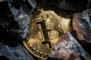 Bitcoin mining and cryptocurrency concept with a golden coin submerged in black stones compared to the traditional gold mining