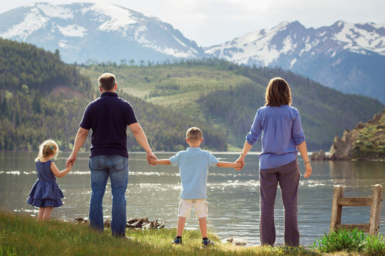 back of family holding hands looking at lake and mountains