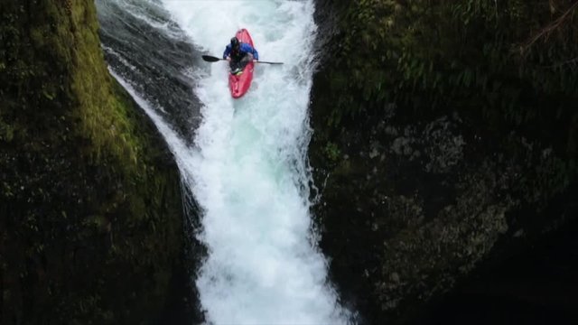 Handheld shot of whitewater kayaker descending from waterfall at forest