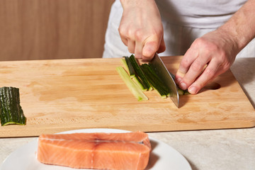 Chef making sushi rolls. Cutting cucumber and salmon fish