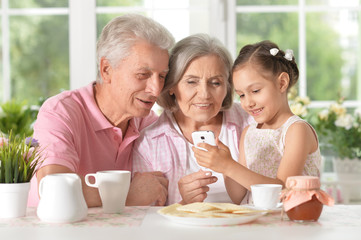 Obraz na płótnie Canvas grandparents with granddaughter using smartphone
