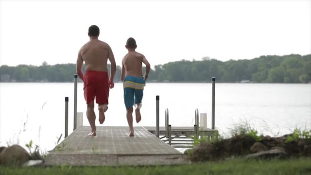 Rear view of father and son jumping from pier in lake