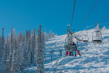 The lift raises two snowboarders to the mountain. The Sheregesh Ski Center. Winter. Russia.